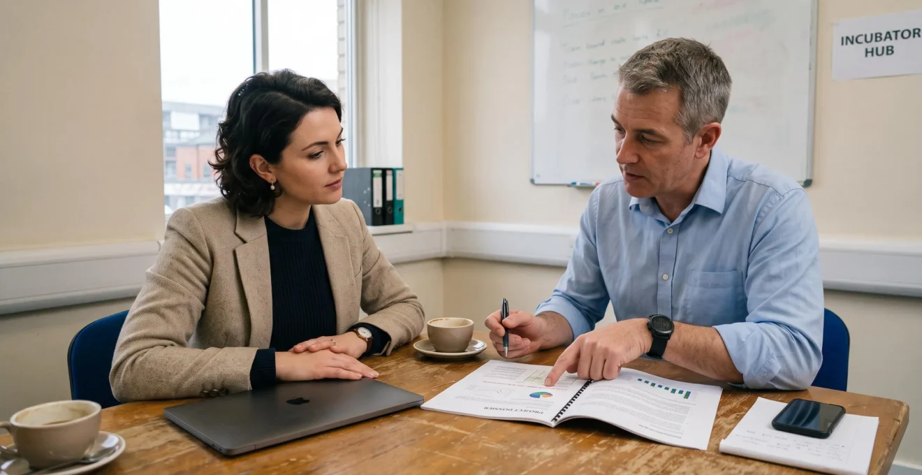Une entrepreneuse présente un dossier de financement à un conseiller qui pointe une page du document lors d'une réunion dans un incubateur.